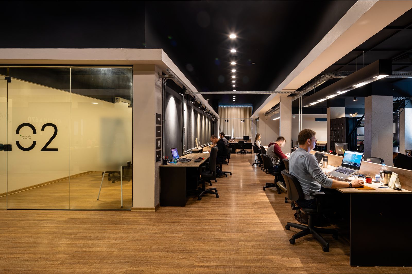 Área compartilhada do Oficina670 com estações de trabalho e oficineiros trabalhando